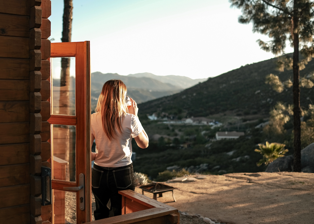 girl drinking coffee on tiny house porch - HipCamp Glamping