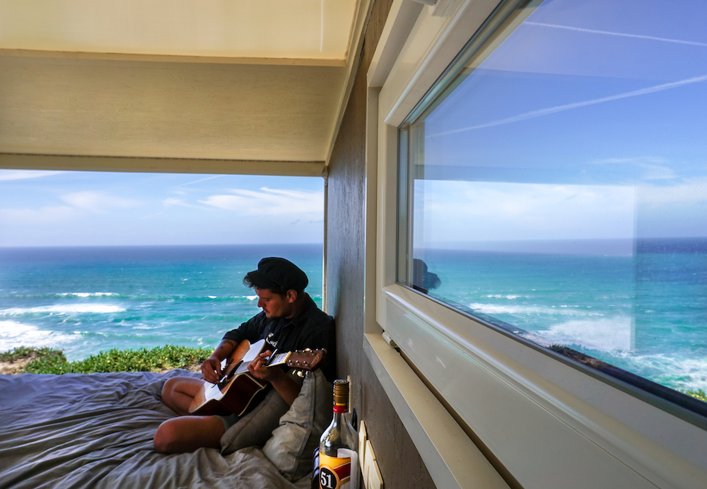 man playing guitar by ocean - off the main road