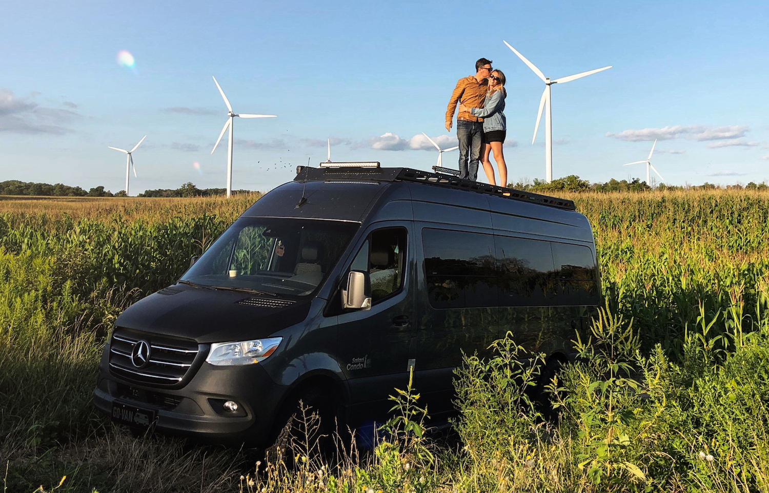 couple in sprinter van in a field with wind turbines